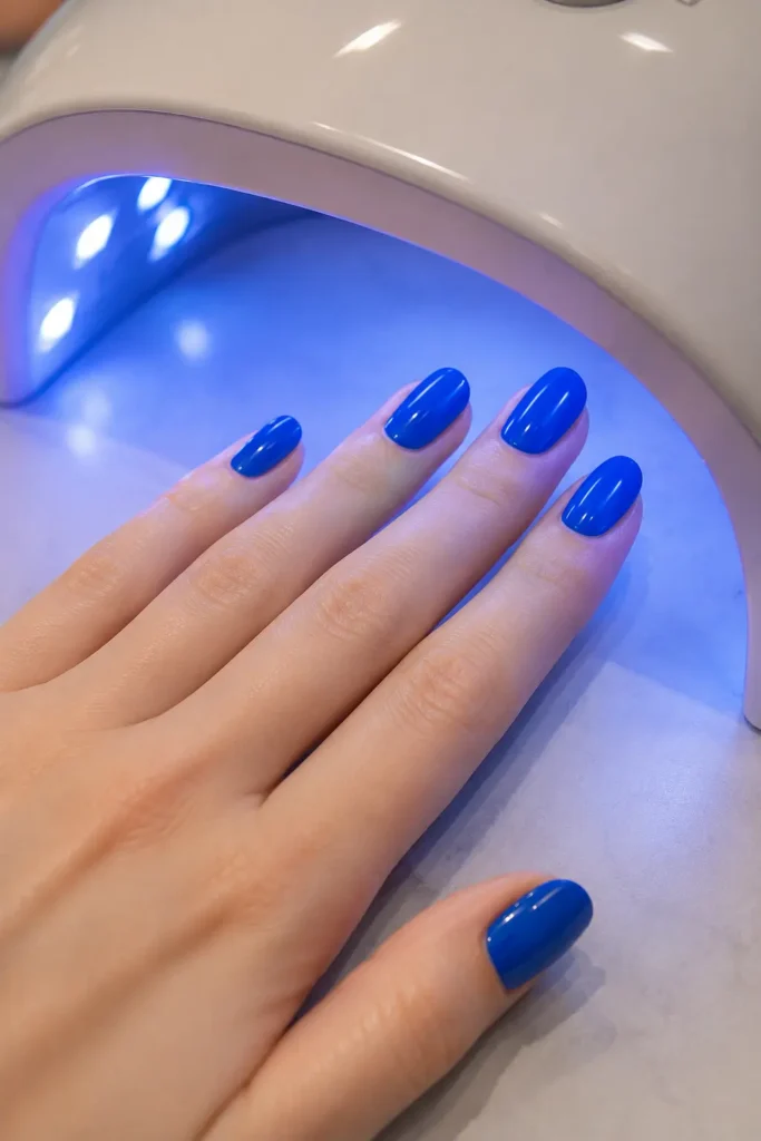 Hand mit blauen Nägeln unter UV-Nagellampe beim Aushärten